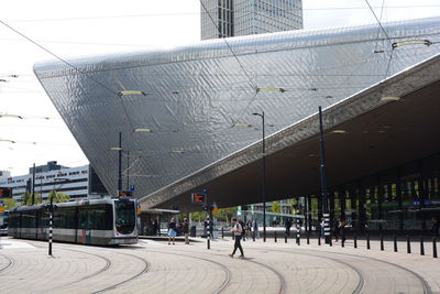 People on street by modern buildings in city against sky