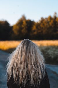 Rear view of woman with blond hair standing at park during sunset