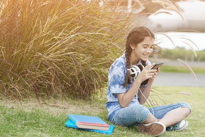 Full length of young woman using phone while sitting on field