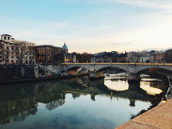 Bridge over river by buildings against sky in city