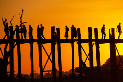 People walking across u-bein bridge on lake taungthaman at sunset.