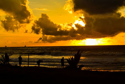 Silhouette people on beach against sky during sunset