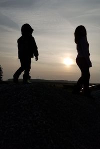 Silhouette children standing against sky during sunset