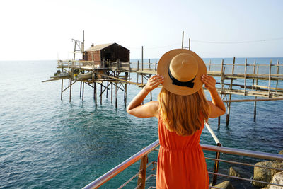 Back view of young woman enjoying view of trabucco an old fishing machine on adriatic sea, italy.