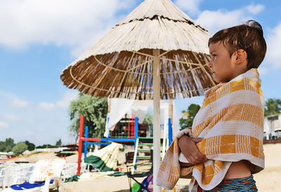 Side view of a boy holding umbrella against sky