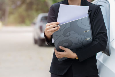 Midsection of woman holding paper while standing by car on street