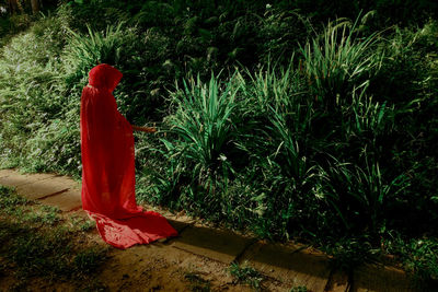 Woman wearing red riding hood cape while standing by plants