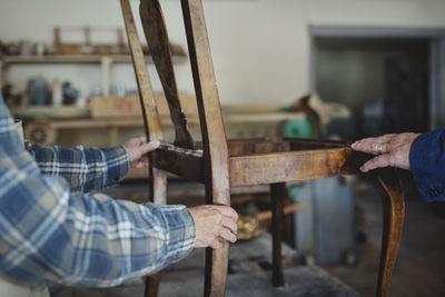 Cropped image of owner showing wooden chair to customer at workshop