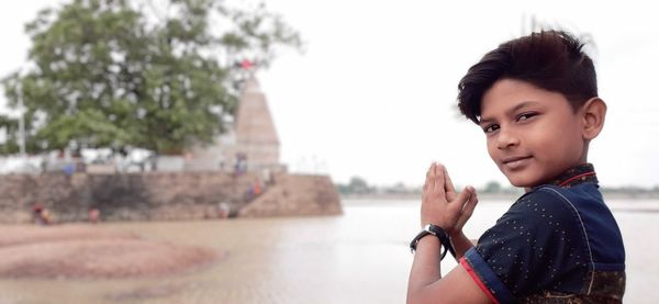 Portrait of cute boy with hands clasped against temple and sky