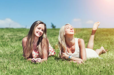 Happy friends lying on grass against sky