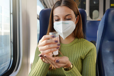 Business woman on train with mandatory face mask using alcohol gel sanitizing hands