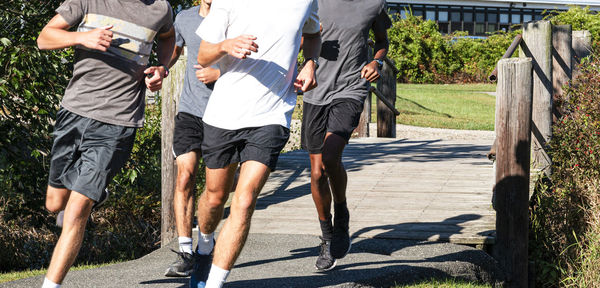 Four cross country runners on a path crossing a wood bridge running together making a left turn.