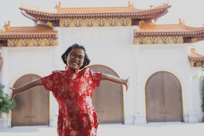 Portrait of cheerful girl with arms outstretched against temple