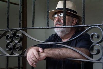 Bearded man, hat and black t-shirt looking through a window