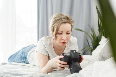 Young woman using mobile phone while lying on bed at home