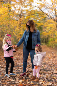 Smiling girls with grandmother wearing mask standing in forest during autumn