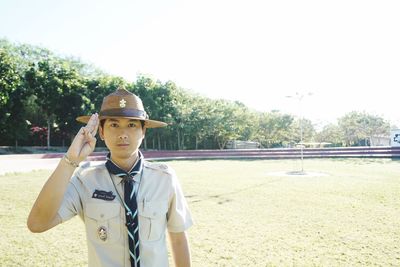 Portrait of police officer saluting while standing on field