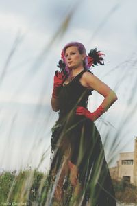 Female model standing in black dress on field against sky