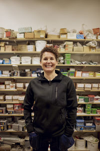 Portrait of happy mature female worker standing in front of rack at hardware store