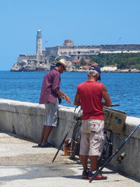 Rear view of man standing on retaining wall by sea against clear sky