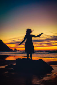 Silhouette woman standing at beach against sky during sunset