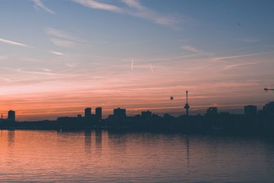 Scenic view of river by silhouette buildings against sky during sunset