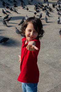 Portrait of boy gesturing while standing on footpath against birds