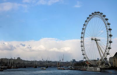 Ferris wheel by river in city against sky