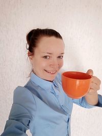 Portrait of smiling woman holding drink against wall