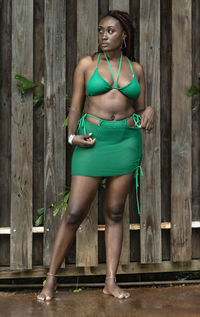 Beautiful jamaican girl in a green swimsuit against wooden fence