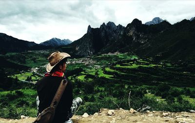 Rear view of man sitting while looking at landscape against sky