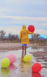 Rear view of man with balloons in water against sky