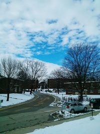 Snow covered road by bare trees against sky