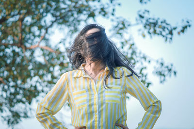 Woman with hair on face standing against tree and sky