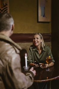 Smiling woman holding smart phone while talking with man sitting at table in restaurant