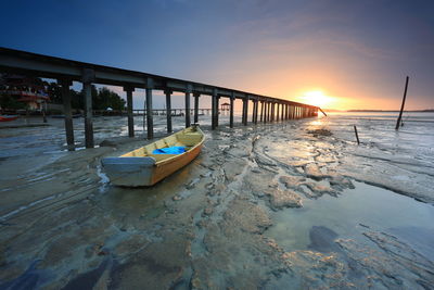 Boat moored on beach against sky during sunset