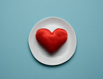 Red heart lies in a white ceramic plate on a blue background, top view