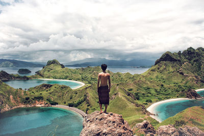 Rear view of shirtless man standing on cliff against sky