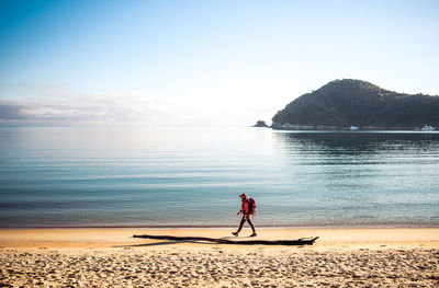 Woman walking down sandy beach with backack with ocean behind her