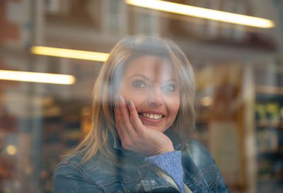 Joyful woman in denim, seen through glass with light reflections