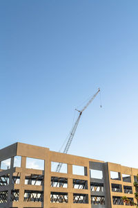 Low angle view of crane by building against clear blue sky