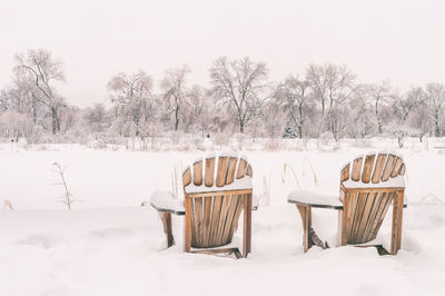 Empty chairs on snow field against clear sky