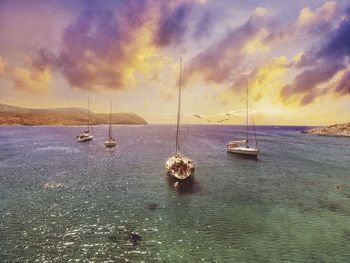 Sailboats moored on sea against sky during sunset