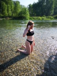 Woman kneeling at lakeshore against trees