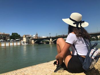 People sitting on bridge over river against clear sky