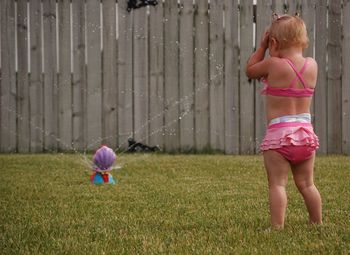 Girl playing by sprinkler on field