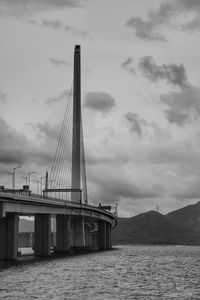 View of suspension bridge over sea against cloudy sky