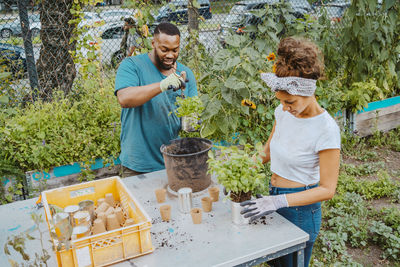 Young male and female farmers planting flower in pot at organic farm