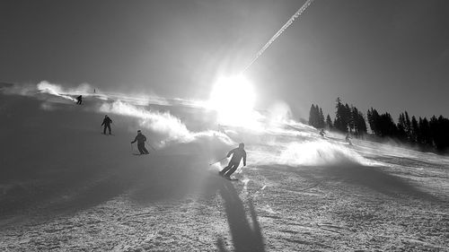 People skiing on field against sky during winter