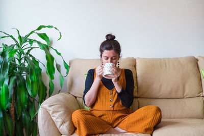 Woman having drink while sitting on sofa at home